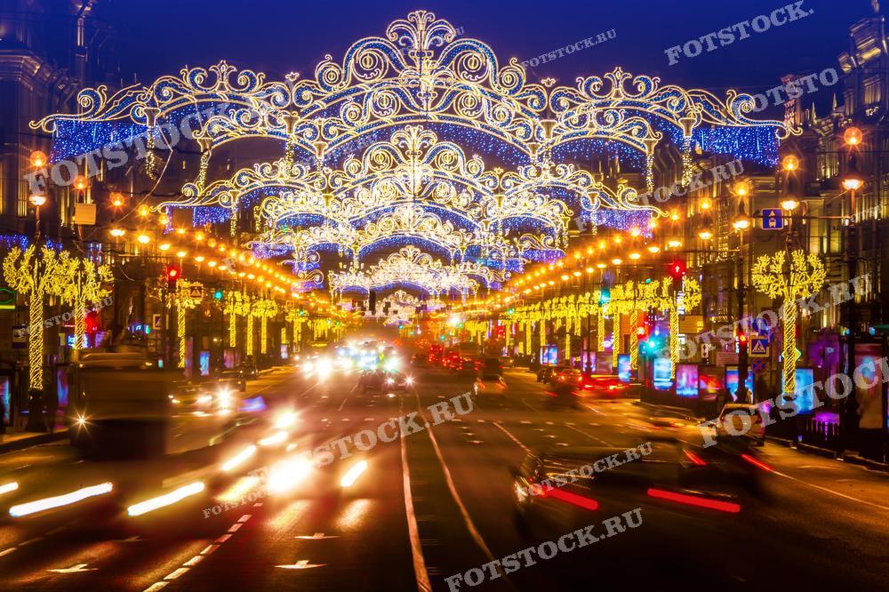 На фотографии изображен Невский проспект в Санкт-Петербурге, украшенный новогодней иллюминацией. Видны движущиеся автомобили и праздничные огни. Фото может использоваться для праздничных открыток, туристических буклетов и рекламных материалов.